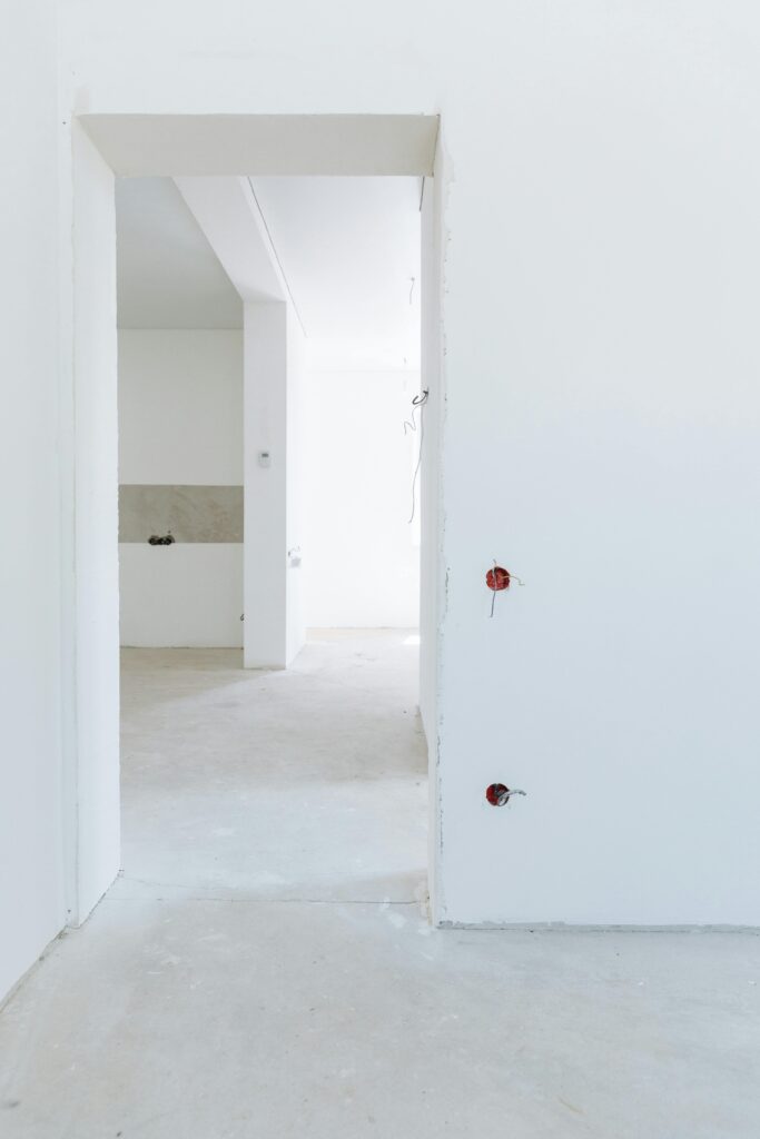 Bright unfinished room with white walls and exposed wiring, showcasing modern interior design potential.